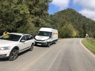 Dodávka mobilného pneuservisu pri aute na okraji cesty pod zalesneným kopcom
