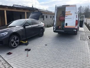 Výmena kolesa na dvore pred domom, v pozadí otvorená dodávka s kompresorom
